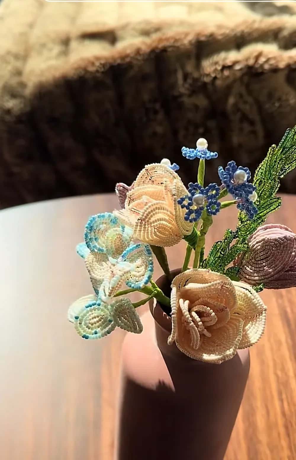 Beaded cream roses, pale blue blossoms and muscari stems in a dark clay vase on a wooden table
