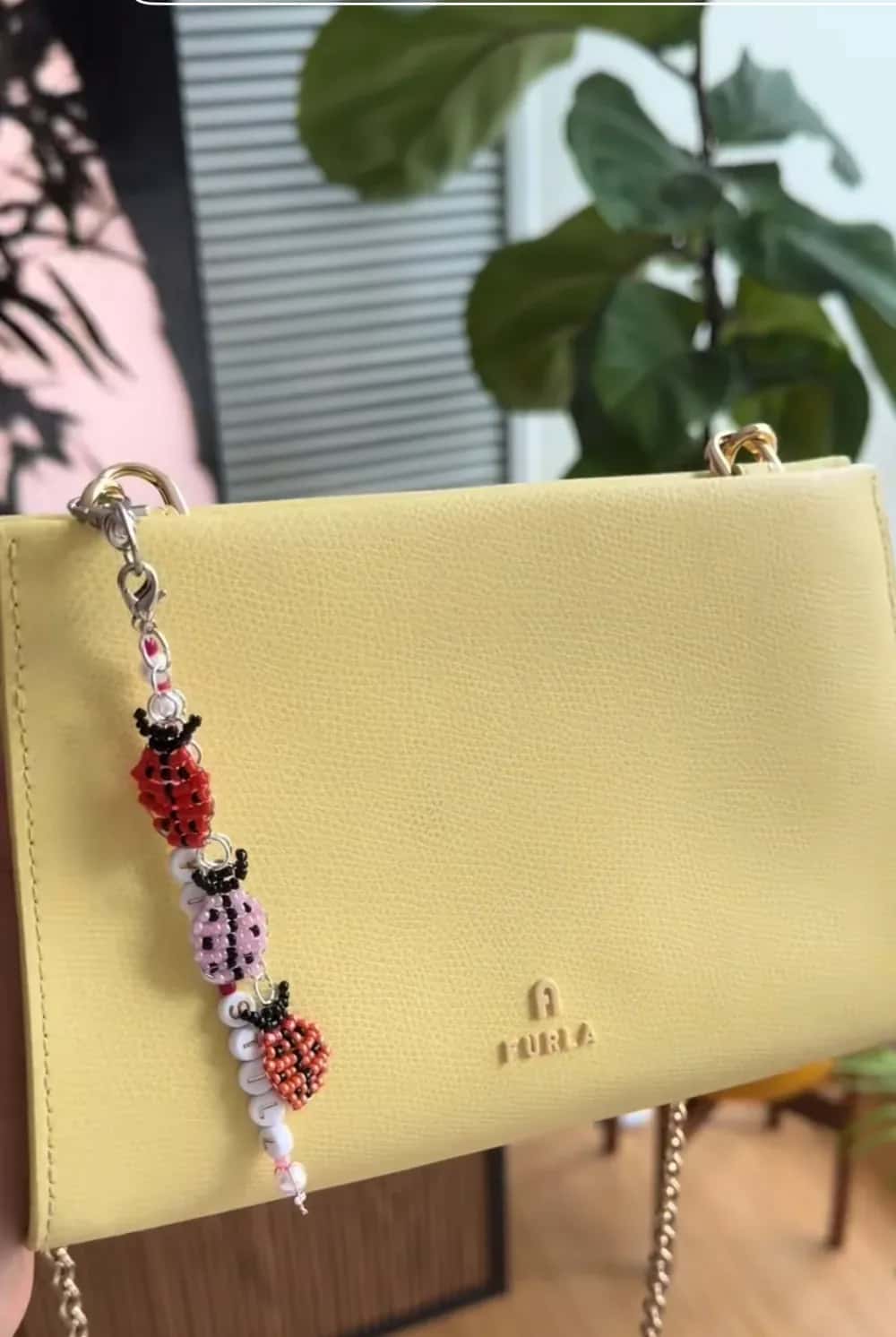A bag charm of beaded ladybugs and letter beads clipped to a yellow leather bag against a city skyline