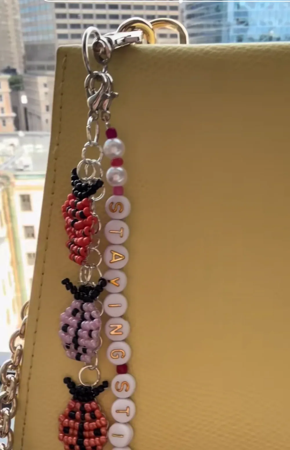 A beaded ladybug and blossom bag charm clipped to a pale yellow leather handbag