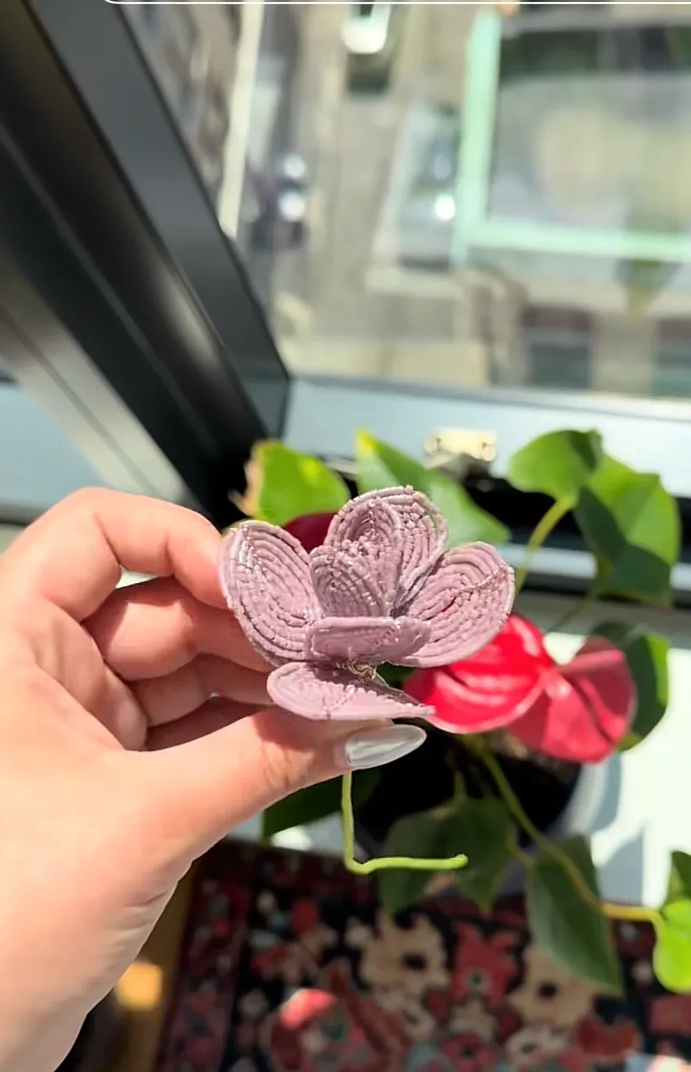 A hand holding a single beaded mauve flower with layered petals